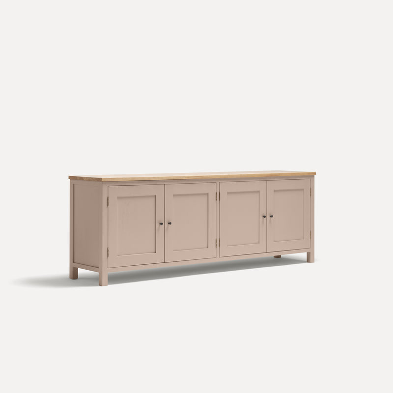 Pink painted four door shaker style sideboard with black metal door knobs and oak worktop. Shown at an angle.